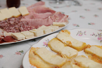 dettagli di alcuni piatti su un tavolo, coperto da una tovaglia chiara,  con vari antipasti a base di salumi affettati, formaggi e polenta