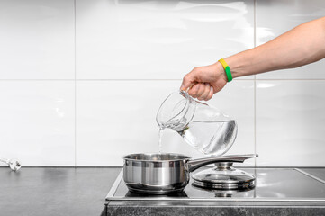 Pour water from a jug into the food that is boiling in the pot on the stove burner.