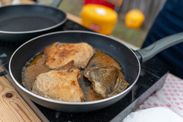 Cooking fish fillets in frying pans outdoors during a sunny summer afternoon gathering