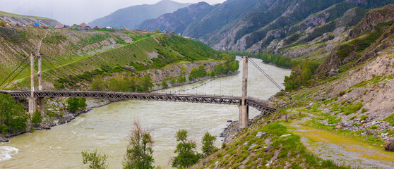 View on Ininsky Bridge across the Katun River in Altai Republic, Russia. Architectural monument, built in 1936 according to the design of S.A. Tsaplin. First double-chain suspension bridge in Russia