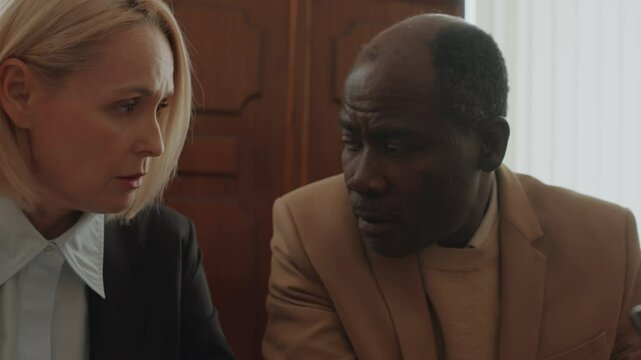 Tilt up shot of Caucasian female prosecutor and Black male plaintiff discussing case during court hearing