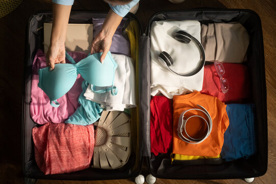 Woman organizes clothing items in an open suitcase, preparing for a vacation or business trip. Careful packing ensures essentials are ready for travel adventures