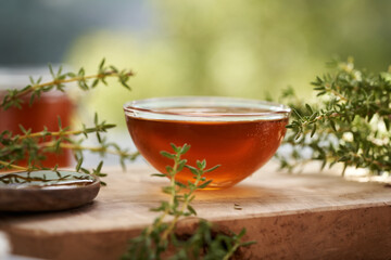 A bowl of herbal syrup with fresh thyme leaves, with green bokeh