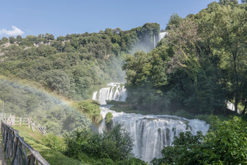 rainbow in mist at tall waterfall amidst lush green vegetation, Marmore, Italy