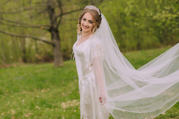 A bride is standing in a field with a white veil and a white dress. She is smiling and looking...
