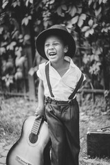 boy dressed in 20s style stands holding guitar and laughs