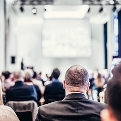 Speaker giving a talk in conference hall at business event. Rear view of unrecognizable people in audience at the conference hall. Business and entrepreneurship concept