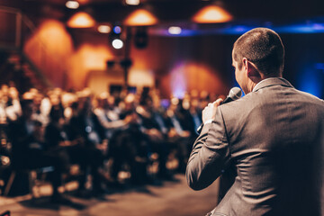 Speaker giving a talk on corporate business conference. Unrecognizable people in audience at conference hall. Business and Entrepreneurship event.