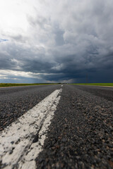 Fototapeta premium narrow rural paved road before a thunderstorm