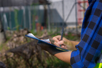A field inspector in a blue plaid shirt meticulously documents findings on a clipboard during an...