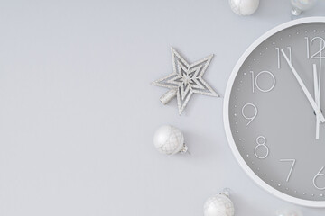 Creative Christmas layout made with silver Xmas baubles, star and gray and white wall clock on gray background. Minimal Christmas eve or New Year idea. Flat lay composition.