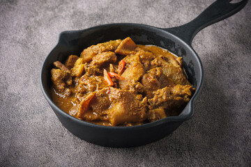 Spicy and aromatic traditional Indian goat curry served on a black pan.