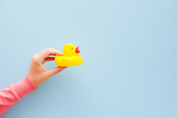 Woman's hand with yellow rubber duck toy for bath on light blue background with copy space