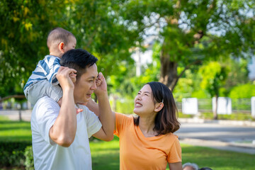 Asian family and baby are in the grass. Everyone looks happy.