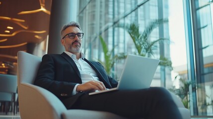 Fototapeta premium Professional man working on laptop in modern office with large windows during daylight hours