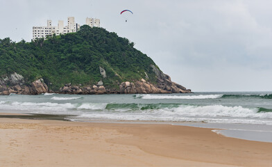 The Tombo Beach of Guaruja, SP, Brazil. The view of the beach with no people, hills in the background, and a paraglider flying in the sky.