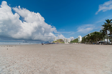 Morning at Enseada Beach on a beautiful day with some clouds, a wide view of the beach sand, the sea, and the hills in the background.  Guaruja - SP, Brazil.