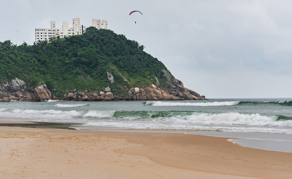 The Tombo Beach of Guaruja, SP, Brazil. The view of the beach with no people, hills in the background, and a paraglider flying in the sky.