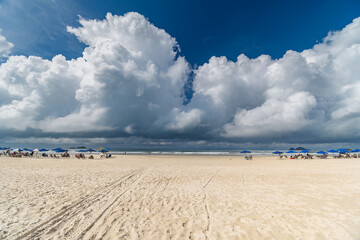 Morning at Enseada Beach on a beautiful sunny day with some rain clouds around, view of the beach sand and the sea. Guaruja - SP, Brazil.