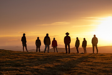 Big group of diverse silhouettes of people or tourists are standing at sunset mountain top