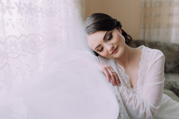A woman in a white gown is sitting on a couch. She is wearing a veil and has her head covered with a flowery headpiece