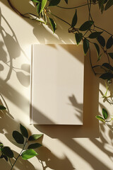 Photo of a minimalist blank journal on an elegant white table with sun rays and shadows. Top View of personal planner  Mockup paper notebook design with leaves and natural sunlight