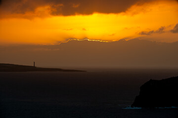 Päikese peegeldus pilvede taga, mis annab teed ööle, mille tunnistajaks on Faro de Buenavista tuletorn.