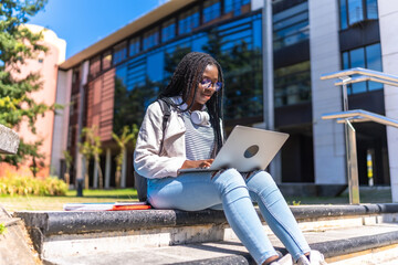Focused african university student using laptop sitting on outdoors staircases