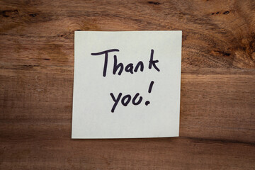 A thank you note is written on a piece of paper and placed on a wooden surface. The note is written in black and white and has a positive and appreciative tone. Concept of expressing gratitude