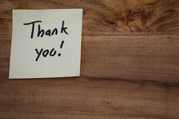 A thank you note is written on a piece of paper and placed on a wooden surface. The note is written in black and white and has a positive and appreciative tone. Concept of expressing gratitude