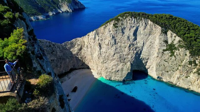 Female tourist at viewpoint overlooking Navagio or Shipwreck Beach, aerial
