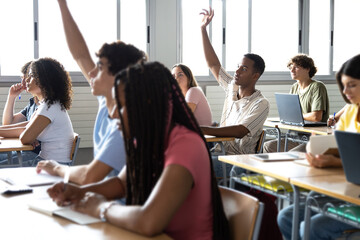 Teen males raising hand to ask question about lesson in classroom.Group of multiracial high school...