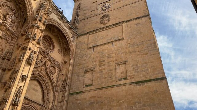 We see one of the doors of the Salamanca Cathedral with a camera elevation, we visualize one of the most imposing towers, the bell tower with a clock and a shield with its stepped bell towers.