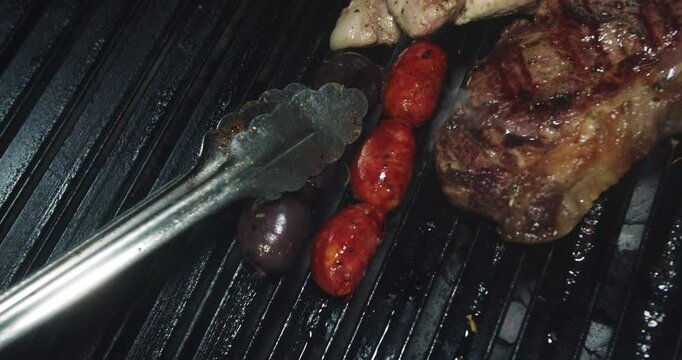 Beautiful camera shot of tongs handling a chorizo and blood sausage on a charcoal grill lit with fire to cook a Venezuelan barbecue in a restaurant.
