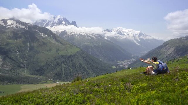 Scenic view of hiking couple on the Mont Blanc hiking trail, surrounded by the towering peaks of the Alps in middle of grassy field
