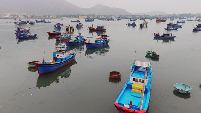 Fleet of bright coloured fishing boats moored in misty calm estuary, Thap Cham, Vietnam. Drone flyover.