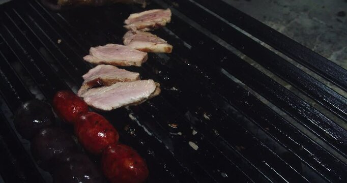 Beautiful slow motion shot of a chef neatly arranging different half-grilled pork steaks on a grill supported with tongs inside a restaurant kitchen.