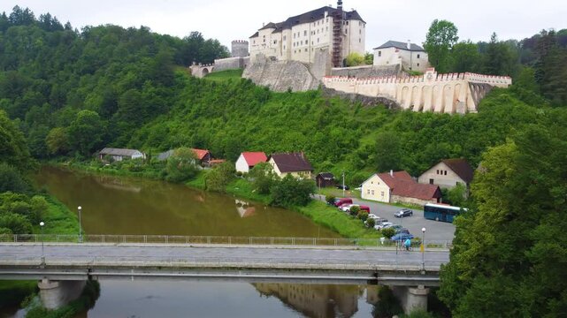 Cesky Sternberk Castle overlooks a river and village, surrounded by lush green hills and forests