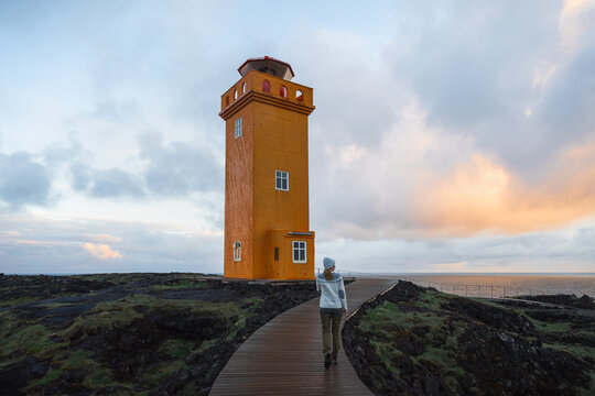 Woman standing in front of orange lighthouse in Iceland