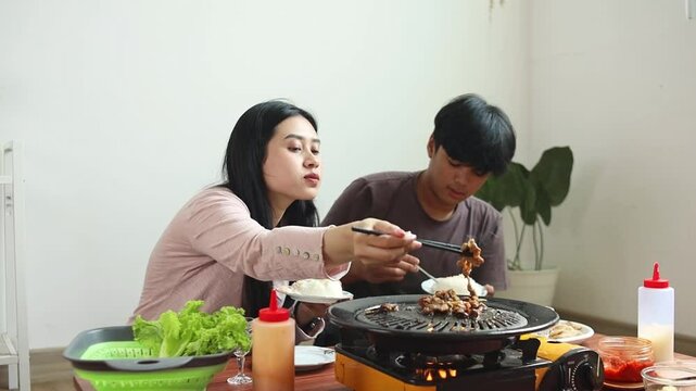 Young Asian Man And Woman Eating Korean Barbaque Together Using Chopstick
