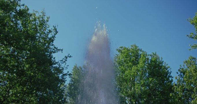 Water from fountain shooting high into the air, framed by lush green trees against a clear blue sky in Zrinjevac Park, Zagreb