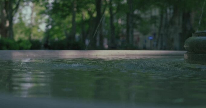 Water ripples in a fountain at Zrinjevac Park, Zagreb, with soft sunlight filtering through the trees in the background