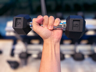 hand gripping dumbbell with a strong, determined hold. The background features a blurred view of...