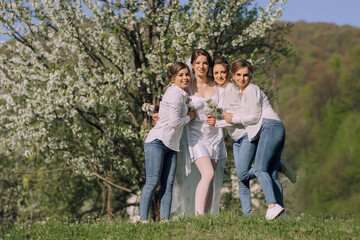 A group of women are posing for a picture in a field of white flowers. The bride is wearing a white dress and is surrounded by her bridesmaids. Scene is joyful and celebratory