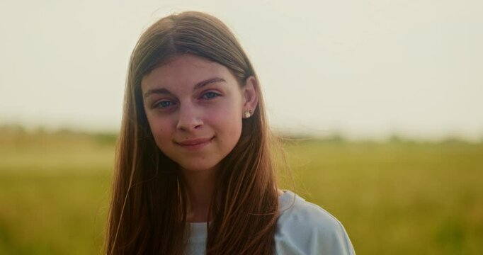 Close up portrait of young brunette girl turning her head, looking at camera and at the sky. Landscape scenery, windy day, yellow field, out of city, shy ukrainian teenager. High quality 4k footage