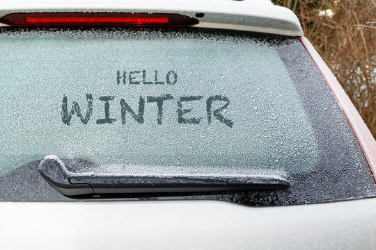 Snow on frozen window of parking  white car in winter. Hello winter text.
