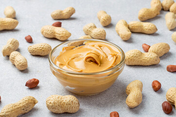 A bowl of peanut butter and whole peanuts laid out in a shell on a gray background. Horizontal.