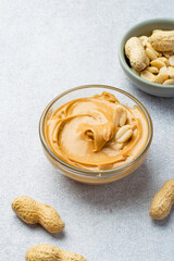 Bowl with peanut butter and whole peanuts on a gray background.