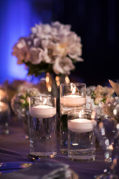 Close-up of floating candles in glass candle holders on table at reception, with flower arrangements in background, Canada