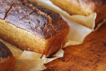 Homemade bread on a wooden kneading board. Bread wrapped in rustic brown paper. Traditional baking with a warm and inviting atmosphere in a cozy kitchen setting. Bread baking craft.